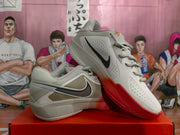 Angled view showing the beige upper, black Swoosh, perforated panels, and red outsole of the Nike sneakers.