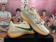 Angled view of a pair of cream Nike sneakers with green Swooshes, orange accents, and textured side panels.