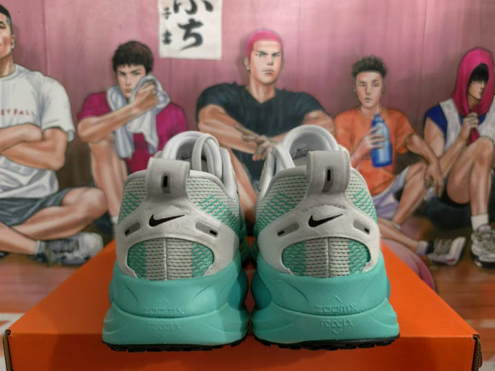 Rear view of gray and green Nike running shoes with black branding, shown on an orange box.
