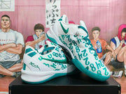 Angled view showing the white and teal Nike sneakers, side Swoosh, graffiti-style upper and heel details.