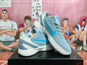 Pair of light blue, white and gray Nike basketball sneakers shown from an angled side view on a black box.