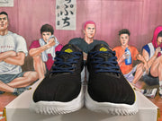 Front view of black basketball sneakers with blue laces, yellow tongue logos, and white textured outsoles.