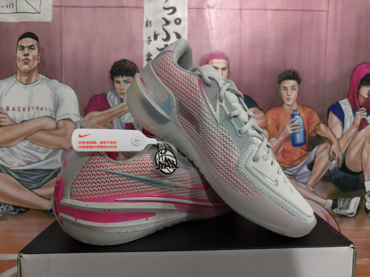 Pair of light grey and pink Nike basketball sneakers displayed on a shoebox, showing the side panels, Swoosh branding and textured upper.