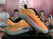 Angled view of orange Jordan basketball sneakers highlighting the side panels, black laces and pale gray outsole.