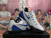 Angled view of the white and blue basketball sneaker pair showing the Swoosh, heel panels, lacing and layered outsole.