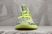 Front view of a lime green knit sneaker with dark patterned detailing and matching laces.