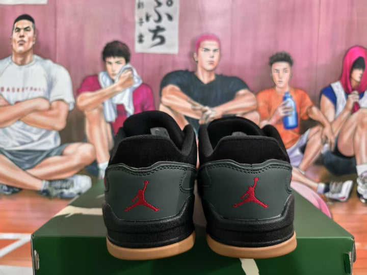 Rear view of black and dark green Jordan sneakers with red embroidered branding and gum-colored outsoles on a green shoebox.