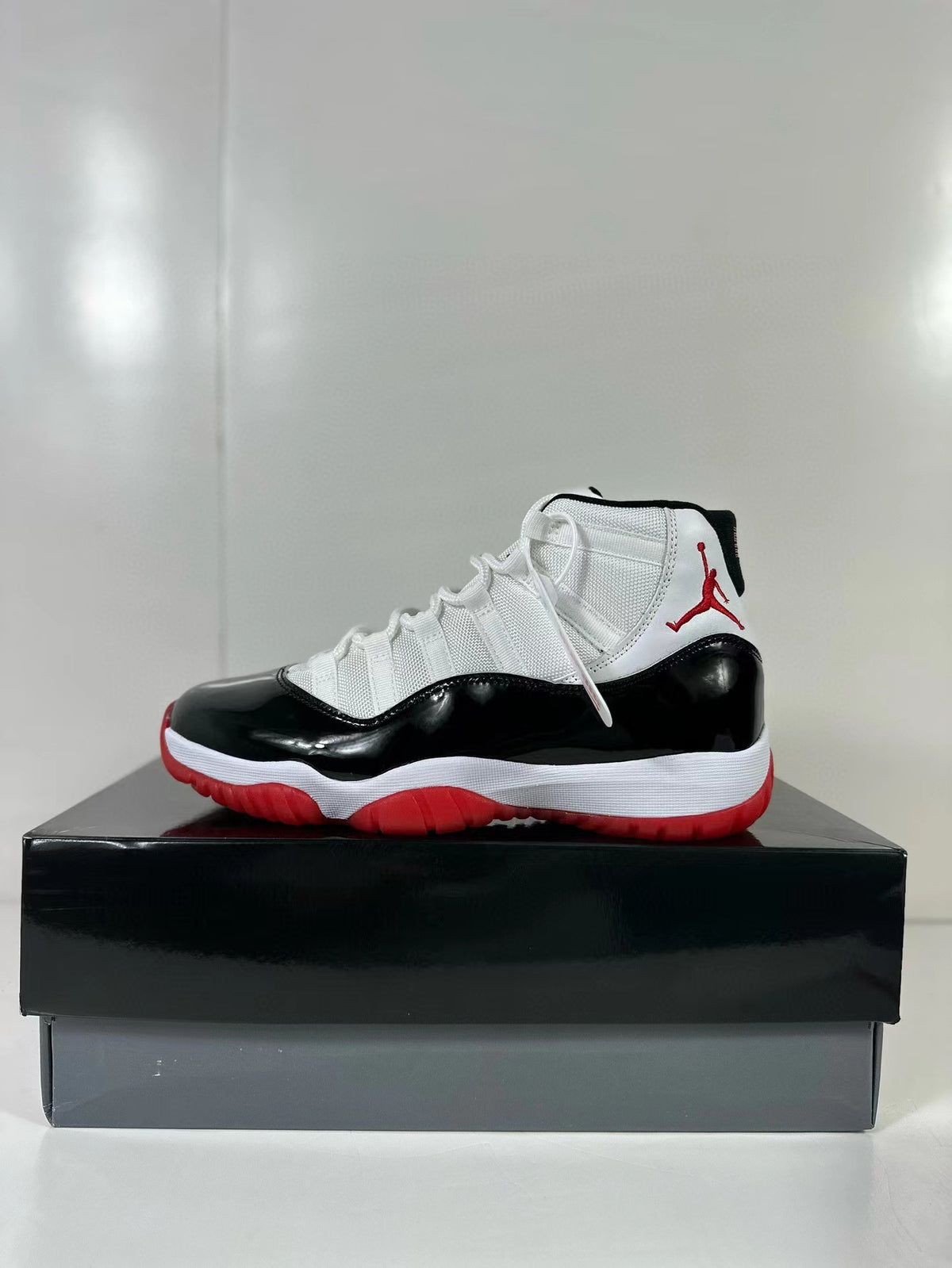 Side view of black, white, and red Jordan Air Jordan 11 Retro sneakers displayed on a black shoebox.