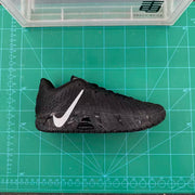 Side profile of a black basketball sneaker displayed on a green cutting mat, showing the silver Swoosh, textured upper and patterned sole.