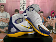 Angled view highlighting the perforated side panel, ankle strap, purple overlays, and yellow trim.