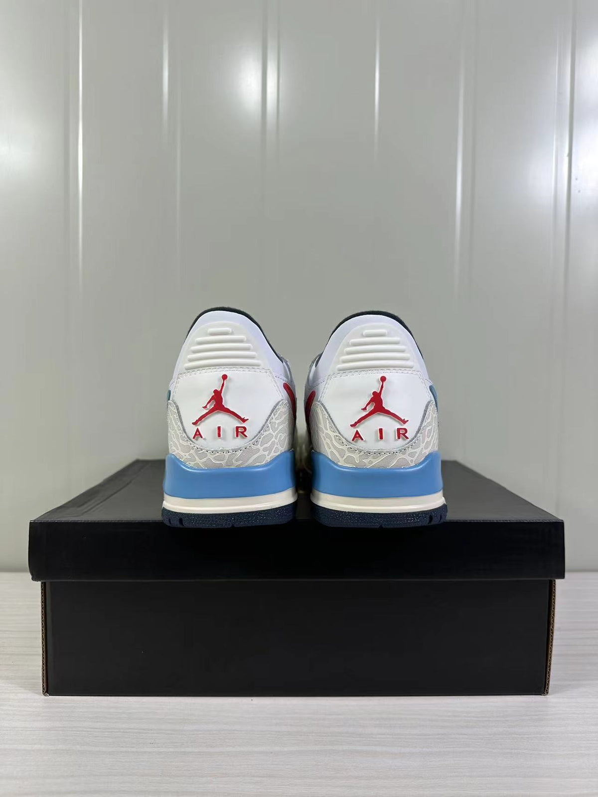 Rear view of the white, blue and red Jordan Legacy 312 Low sneakers on a black box.