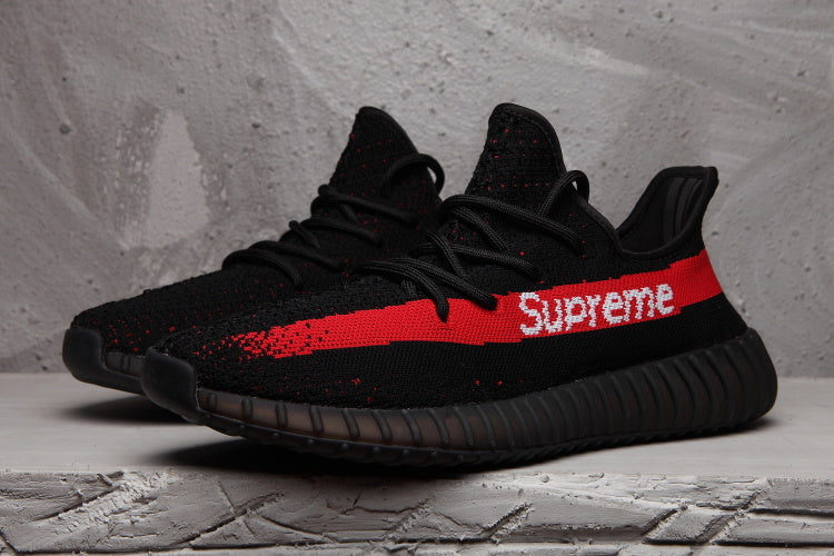 Pair of black knit-style low-top sneakers with red side stripes and white Supreme lettering.