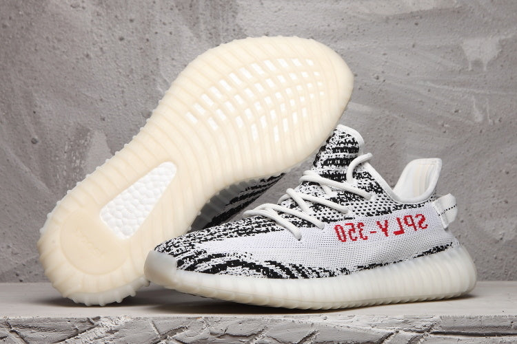 Side view of black-and-white patterned Yeezy 350 V2 sneakers, showing the ribbed off-white sole and red side text.