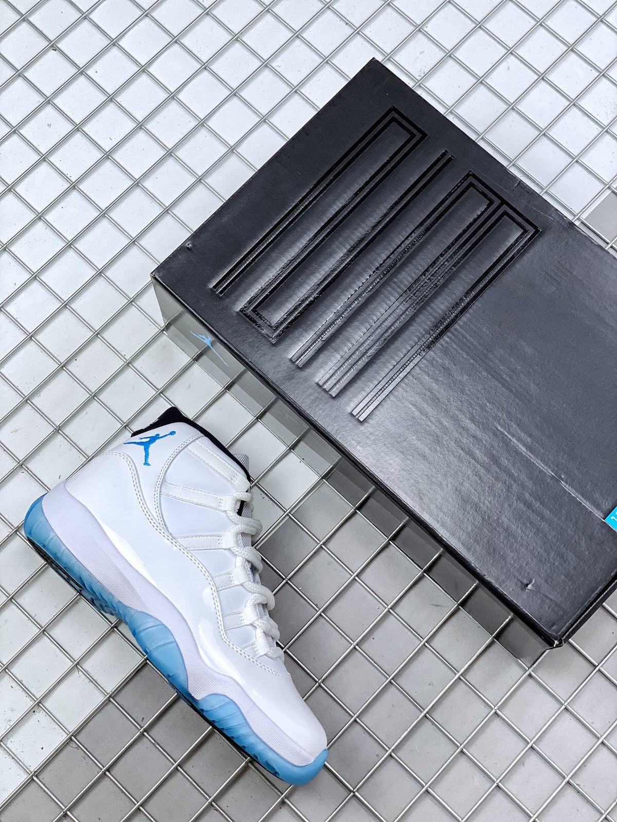 White and blue Jordan 11 sneaker shown beside a black shoebox.