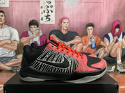 Side view of a Nike basketball sneaker showing black and pink panels, white striped side graphics, orange laces, and a translucent outsole.