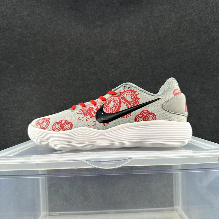 Side view of a light gray Nike low-top sneaker with red dragon-inspired graphics and laces, a black Swoosh, and a white ridged sole.