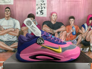 Side view of pink and purple Nike basketball shoes with a gold Swoosh and turquoise accents on a shoe box.