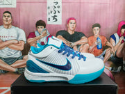 Side view of white Nike Kobe basketball shoe with blue Swoosh, striped panels, and teal outsole.