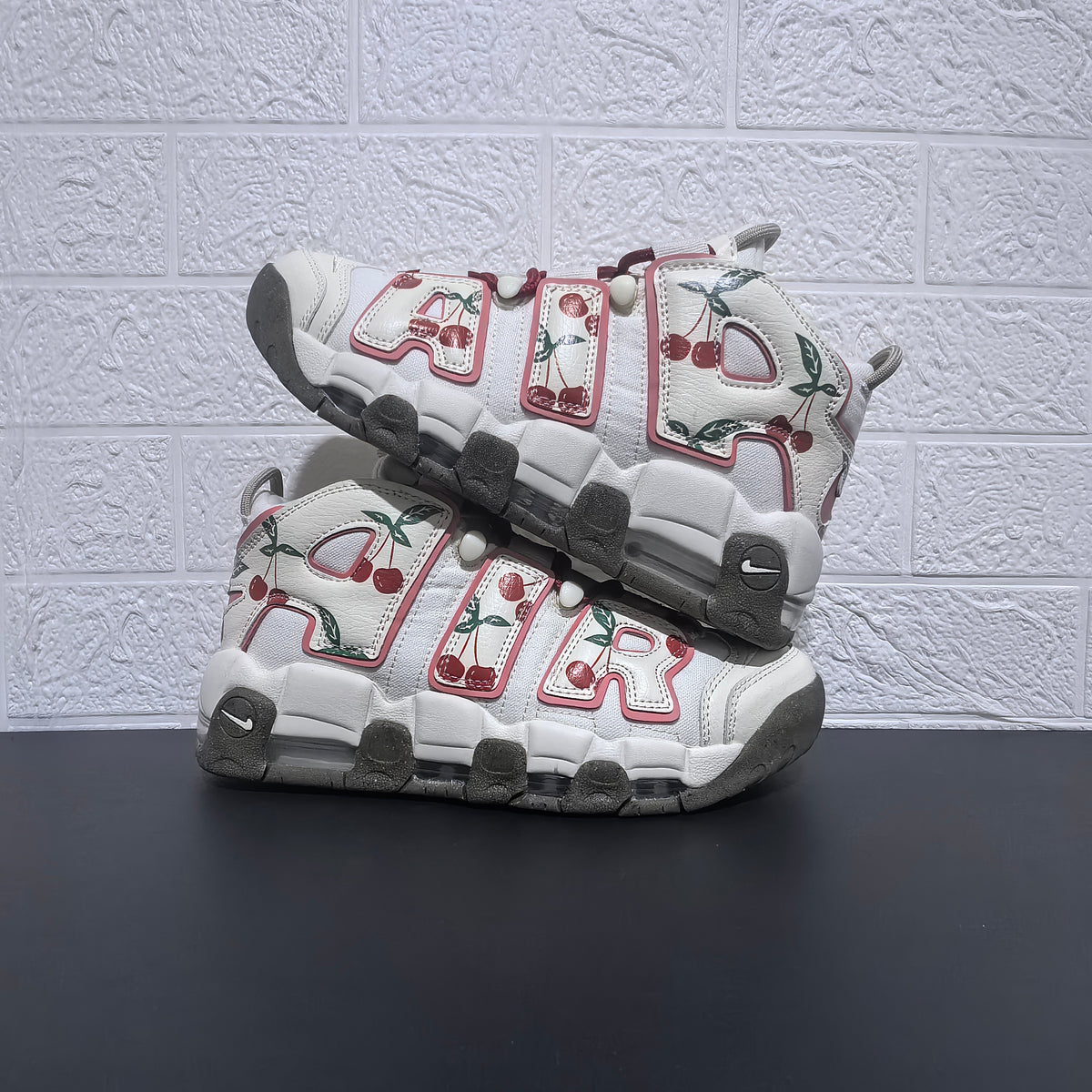 Pair of white Nike Air More Uptempo sneakers with cherry graphics and pink-trimmed lettering