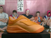 Side profile of a tangerine-orange slip-on sneaker showing the streamlined upper, raised heel, and textured outsole.
