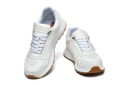 Front view of white Prada lace-up sneakers with perforated toe panels and gum-colored sole accents.