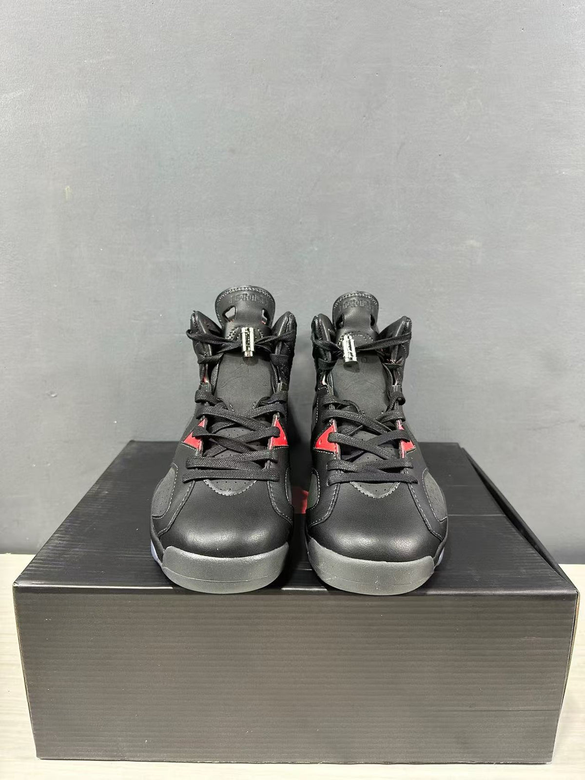 Front view of black Jordan mid-top sneakers with red accents, displayed on a black shoebox.