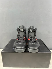 Front view of black Jordan mid-top sneakers with red accents, displayed on a black shoebox.