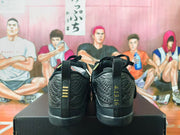 Rear view of black and gold basketball shoes showing heel details and pull tabs.