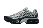 Side profile of grey and black Nike Air Max Plus VII sneakers with orange Swoosh accents and visible air units.