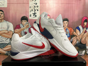 Pair of white Nike basketball shoes showing red Swoosh accents, navy details, and red outsoles.