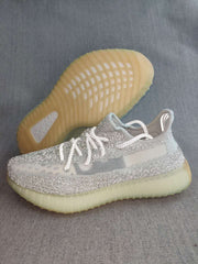 Silver and white sneaker shown beside its translucent yellow-toned outsole.