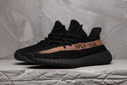 Pair of black Yeezy 350 V2-style sneakers viewed from the front side, showing the lace-up upper and contrasting side stripe.