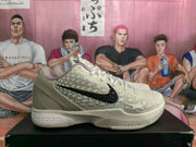 Side view of a cream Nike sneaker with black Swoosh detailing and textured star-pattern panels.