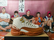 Side view of a cream and brown Jordan 12 high-top sneaker with gold-tone lace hardware.