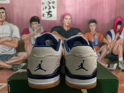 Rear view of gray and dark blue Jordan sneakers with Jumpman logos, white midsoles, and gum-colored outsoles.