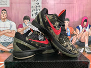 Angled view of paired Nike basketball sneakers showing camouflage panels, red Swooshes, black midsoles and olive heel details.