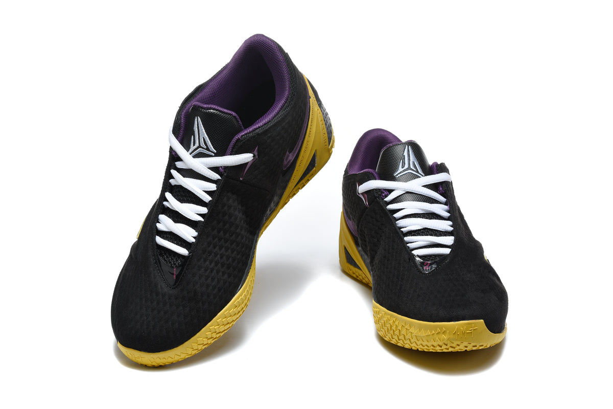 Pair of black low-top Nike Kobe-style basketball shoes with white laces, purple details, and gold-colored outsoles, viewed from the front.