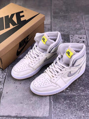 Pair of pearl white Jordan AJ1 high-top sneakers beside a branded shoe box, showing gray side accents and yellow tongue labels.