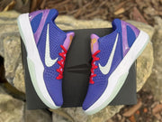 Overhead view of the pair placed on a black box, showing the side branding, purple-blue color scheme, and translucent outsoles.
