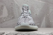 Front view of the gray and white sneaker showing its laces, patterned toe box, and rounded translucent outsole.