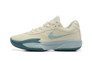 Side profile of a cream Nike G.T. Cut Academy basketball shoe with pale blue Swoosh and midsole accents.