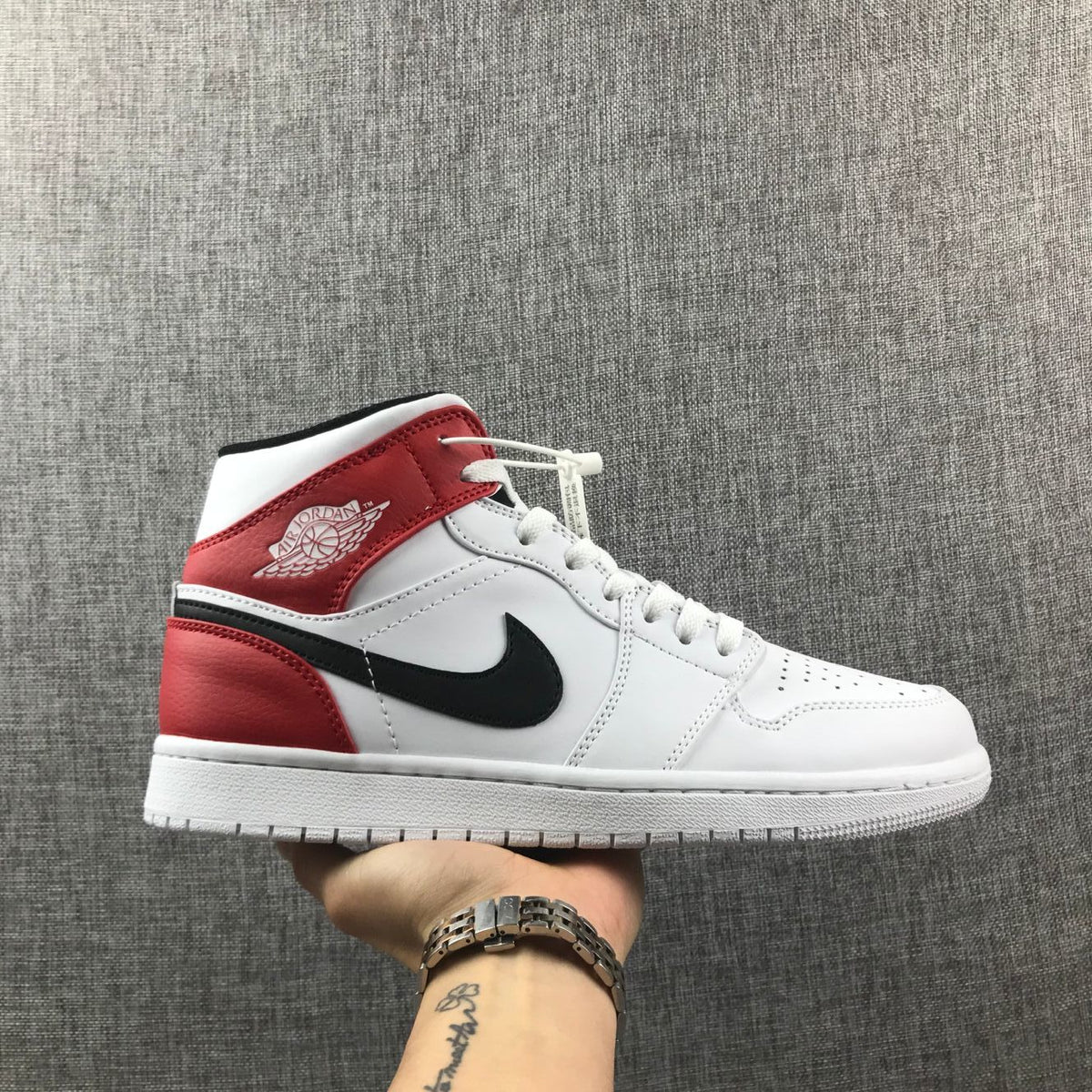 Side profile of a white, red, and black Jordan 1 Mid sneaker with a black Swoosh-style logo.
