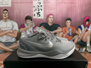 Side view of a gray Nike basketball sneaker showing the Swoosh, Kobe-related side graphics, layered midsole, and outsole.