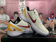 Pair of off-white Nike Kobe basketball shoes with red side logos, gold heel accents, and white soles.