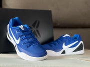 Front three-quarter view of royal blue sneakers showing blue laces, white swooshes, and a Kobe-themed box in the background.