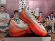 Two white and bright orange Nike basketball shoes arranged at an angle, showing the patterned uppers and red laces.