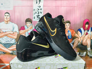 Angled view of black Nike Kobe basketball shoes showing gold-tone Swooshes and glossy black soles