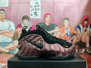 Side profile of a brown Nike Foamposite-style sneaker with black Swoosh detail, orange accent, and textured black sole.