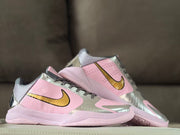 Angled side view of the pink and silver shoes with gold Swoosh branding.