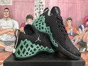 Angled view of the paired black Jordan basketball sneakers displaying the green geometric overlays and textured uppers.
